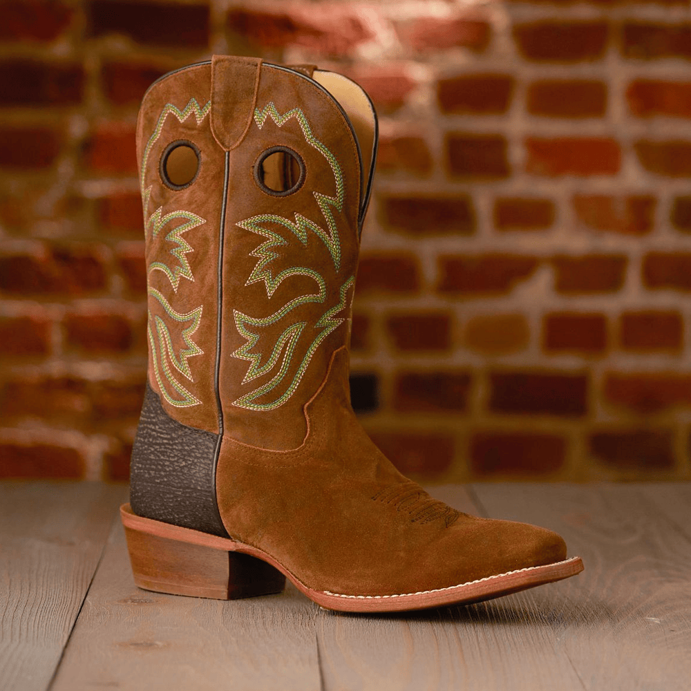 A single Hudson 11” Western boot in Crown in brown in front of a brick wall. Shop final sale. 
